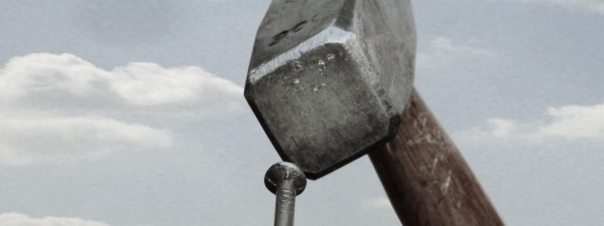 Hammer trifft Nagel auf dem Kopf Hammer trifft Nagel vor blauem Himmel