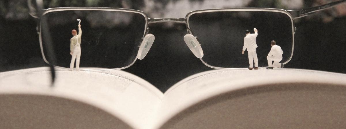 Miniaturfiguren putzen die Gläser einer Brille, die auf einem aufgeschlagenen Buch liegt